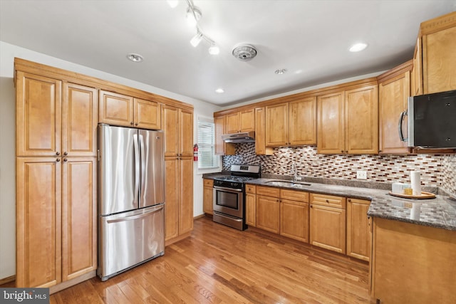 kitchen with dark stone counters, sink, decorative backsplash, light wood-type flooring, and stainless steel appliances