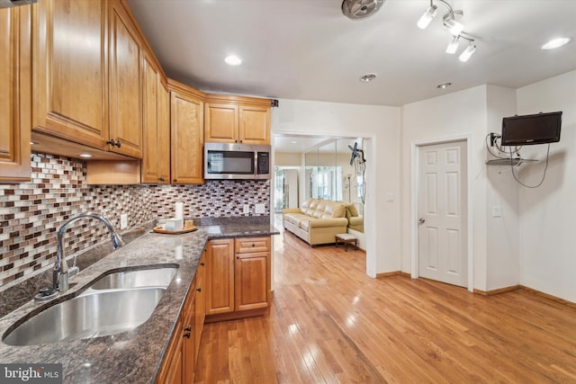 kitchen featuring backsplash, light hardwood / wood-style floors, dark stone counters, and sink