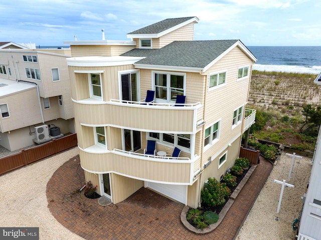 rear view of house featuring a beach view, a shingled roof, a water view, and a balcony