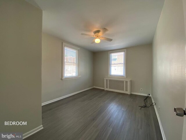 empty room with ceiling fan, plenty of natural light, dark wood-type flooring, and radiator