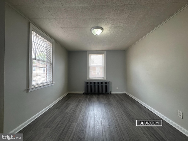 spare room featuring baseboards, dark wood finished floors, and radiator