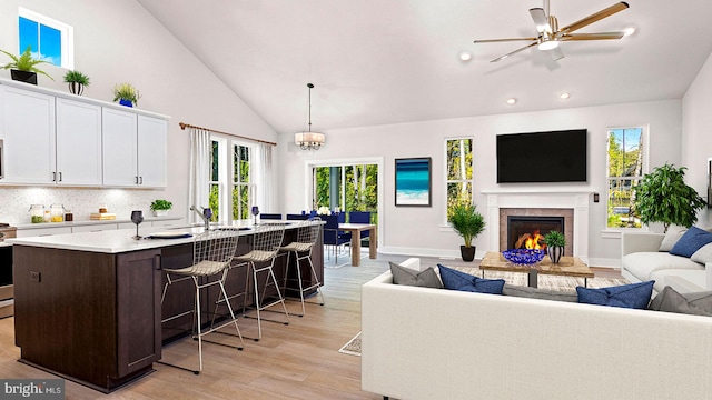 kitchen featuring a kitchen breakfast bar, decorative light fixtures, light wood-type flooring, a fireplace, and an island with sink