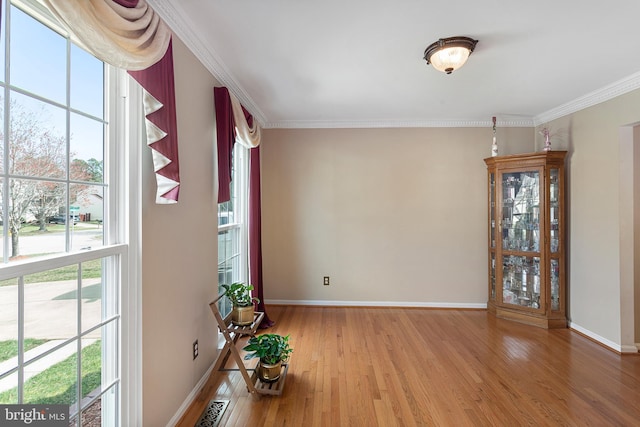 empty room with ornamental molding, wood finished floors, and baseboards