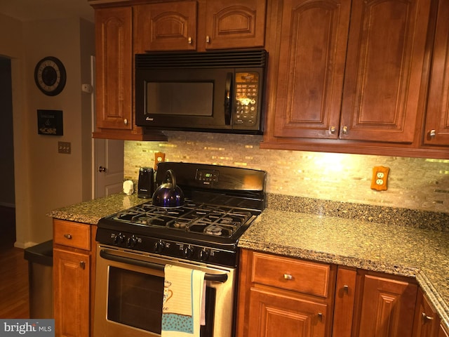 kitchen with black microwave, light stone counters, backsplash, and gas range