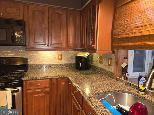 kitchen featuring black microwave, a sink, stainless steel range with gas cooktop, dark stone counters, and glass insert cabinets