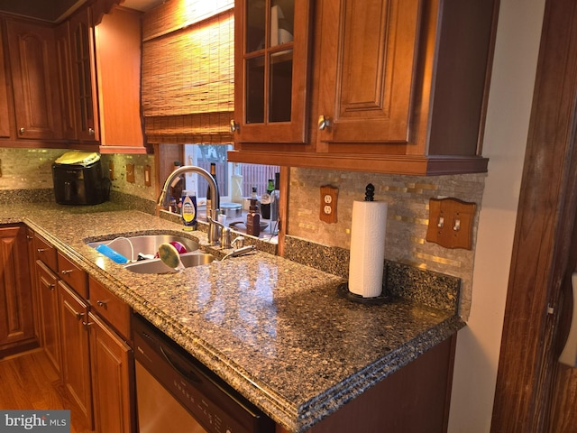 kitchen with wood finished floors, a sink, decorative backsplash, dishwasher, and glass insert cabinets