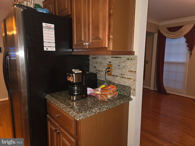 kitchen featuring dark wood-type flooring, ornamental molding, stainless steel refrigerator with ice dispenser, dark stone counters, and brown cabinetry