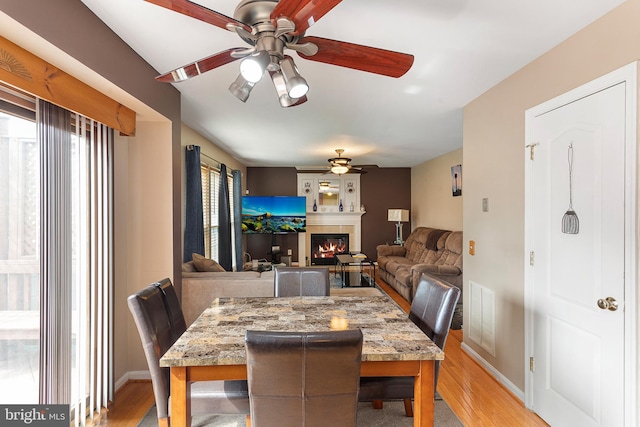 dining room featuring light wood-style floors, a ceiling fan, visible vents, and a tiled fireplace