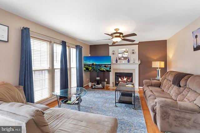 living room with light wood-type flooring, a fireplace with flush hearth, a ceiling fan, and baseboards