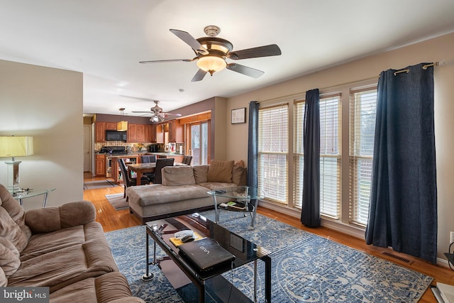 living room featuring light wood-style floors, a healthy amount of sunlight, visible vents, and ceiling fan