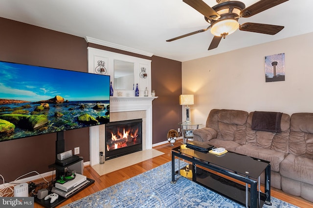 living area with light wood-style flooring, baseboards, ceiling fan, and a fireplace with flush hearth