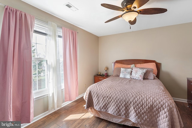 bedroom with a ceiling fan, dark wood-style flooring, visible vents, and baseboards