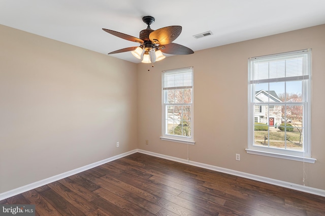 unfurnished room featuring dark wood-type flooring, a ceiling fan, visible vents, and baseboards