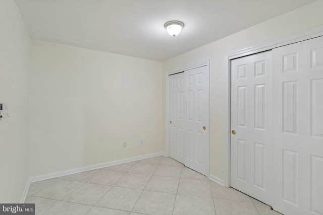 unfurnished bedroom featuring multiple closets, baseboards, and light tile patterned floors