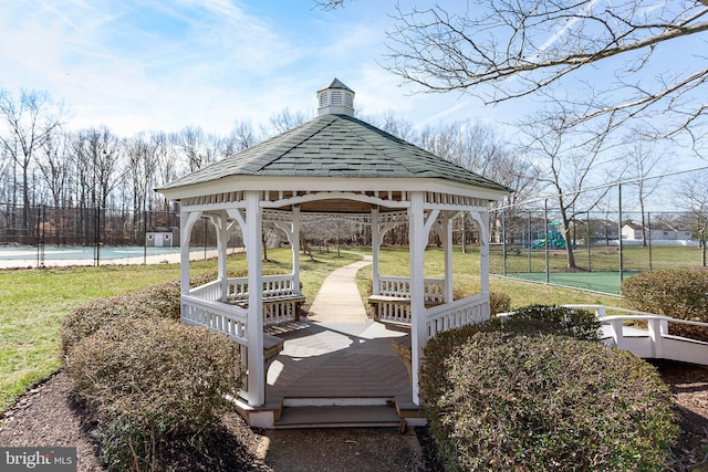 view of community featuring a tennis court, fence, a lawn, and a gazebo