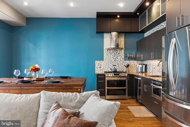 kitchen featuring wall chimney range hood, decorative backsplash, sink, light hardwood / wood-style floors, and stainless steel appliances