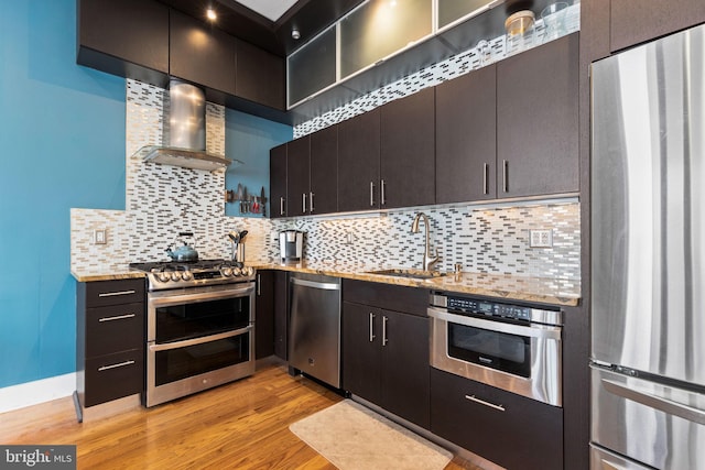 kitchen with wall chimney range hood, tasteful backsplash, light hardwood / wood-style flooring, sink, and stainless steel appliances