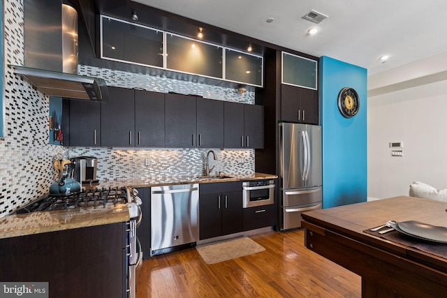 kitchen with backsplash, sink, light hardwood / wood-style floors, wall chimney exhaust hood, and stainless steel appliances