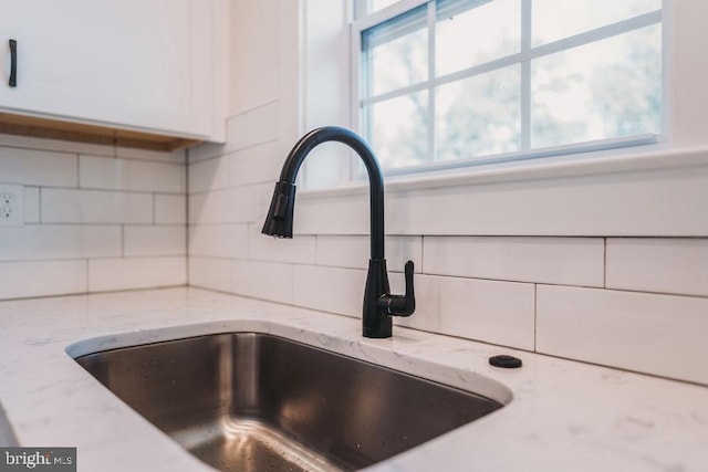 room details featuring decorative backsplash, white cabinetry, sink, and light stone counters