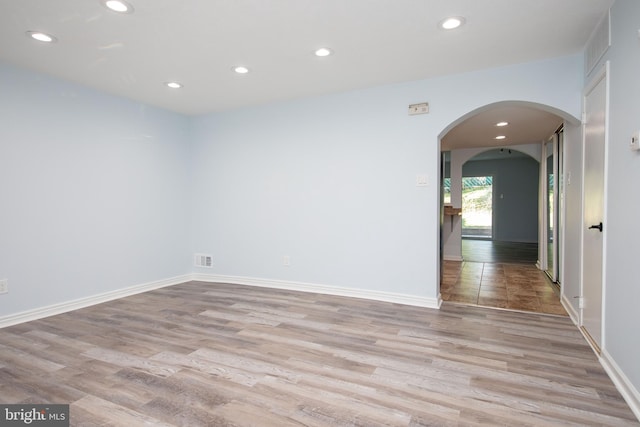 spare room featuring arched walkways, light wood-type flooring, baseboards, and recessed lighting