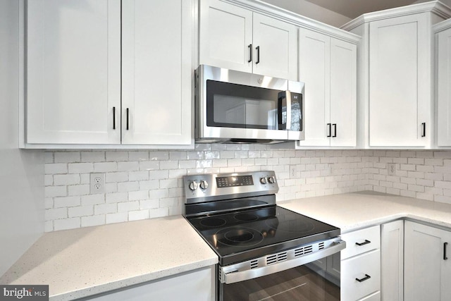 kitchen featuring tasteful backsplash, white cabinets, appliances with stainless steel finishes, and light stone counters