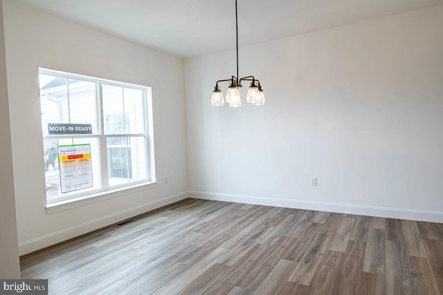 empty room featuring an inviting chandelier, wood finished floors, visible vents, and baseboards