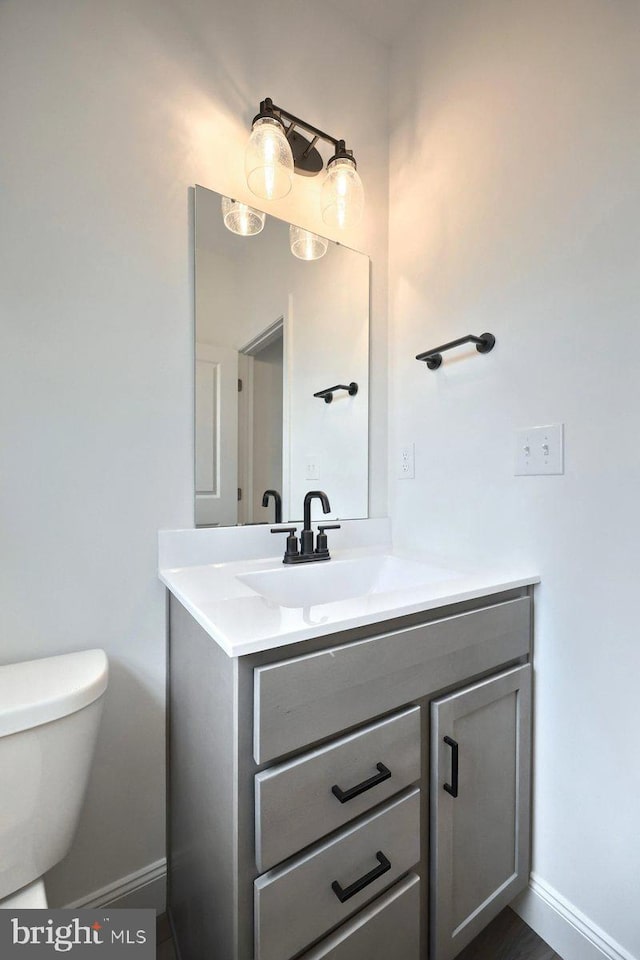 half bathroom with vanity, toilet, and baseboards