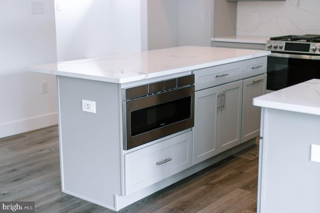 kitchen with light stone counters, a kitchen island, appliances with stainless steel finishes, dark hardwood / wood-style floors, and gray cabinets