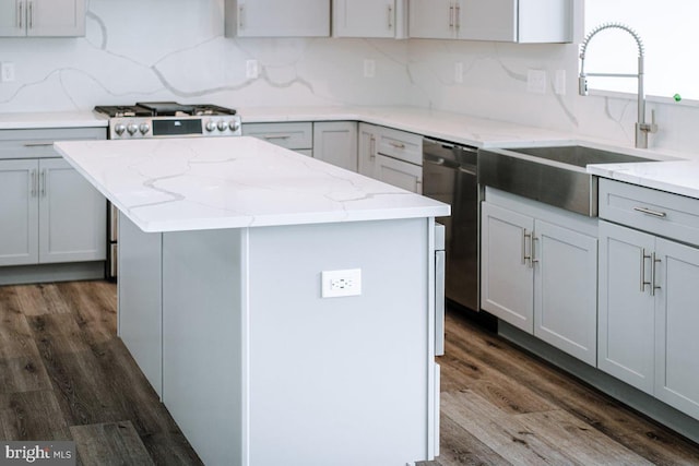 kitchen with appliances with stainless steel finishes, gray cabinetry, backsplash, a center island, and dark hardwood / wood-style flooring