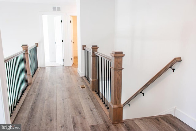 hallway with an upstairs landing, visible vents, light wood finished floors, and baseboards