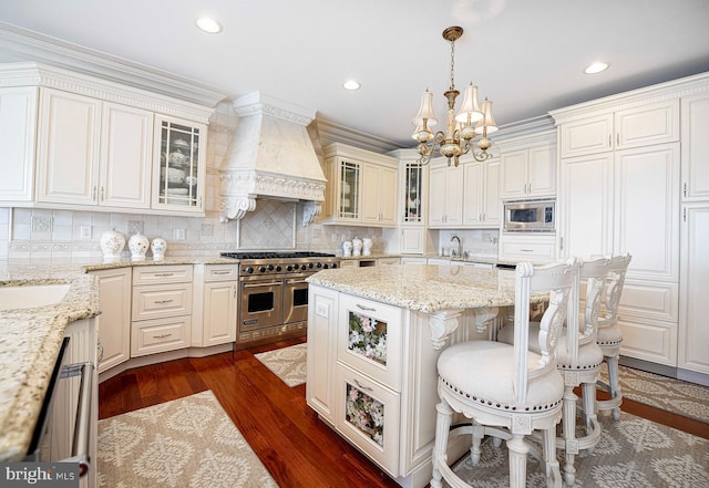 kitchen with light stone counters, pendant lighting, appliances with stainless steel finishes, custom range hood, and dark hardwood / wood-style flooring