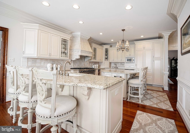 kitchen featuring pendant lighting, a center island with sink, dark hardwood / wood-style floors, and premium range hood