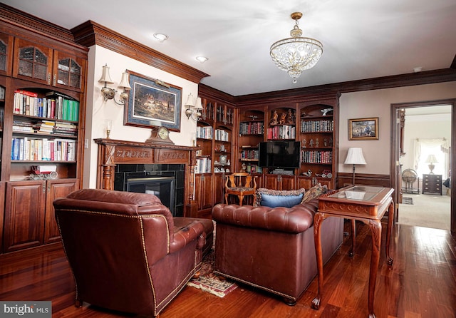 living room with built in features, an inviting chandelier, a fireplace, crown molding, and dark hardwood / wood-style flooring