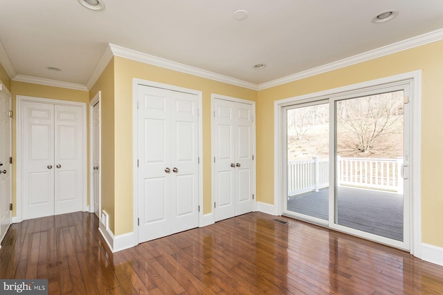 unfurnished bedroom with multiple closets, access to outside, dark hardwood / wood-style floors, and crown molding