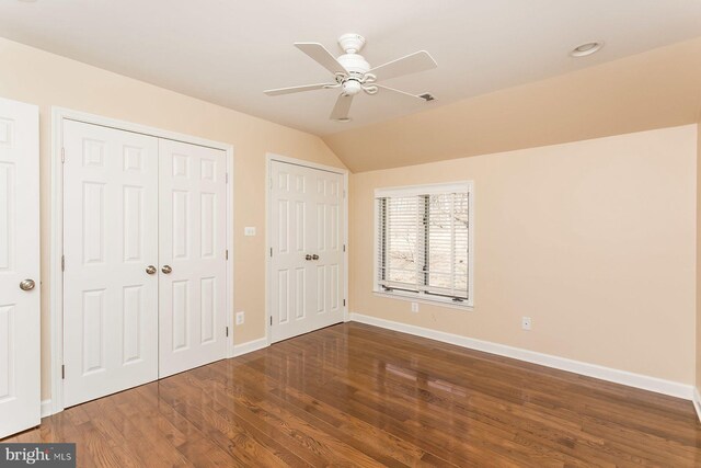 unfurnished bedroom with ceiling fan, two closets, wood-type flooring, and lofted ceiling