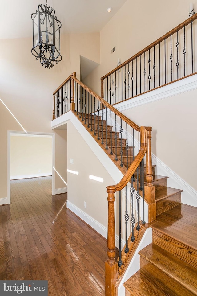 stairway featuring high vaulted ceiling, a chandelier, and wood-type flooring