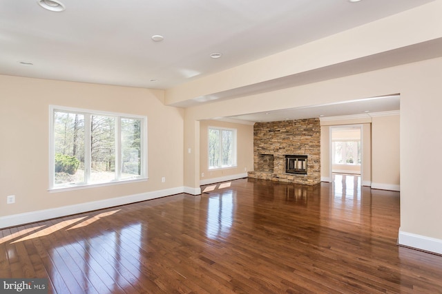 unfurnished living room featuring a baseboard heating unit, a stone fireplace, dark hardwood / wood-style flooring, and a healthy amount of sunlight