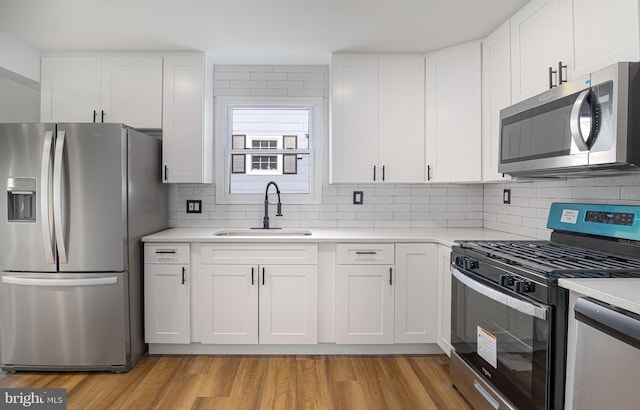 kitchen featuring appliances with stainless steel finishes, sink, backsplash, white cabinetry, and light hardwood / wood-style floors