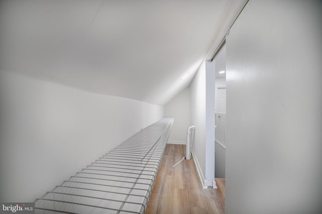 corridor with light hardwood / wood-style floors and lofted ceiling