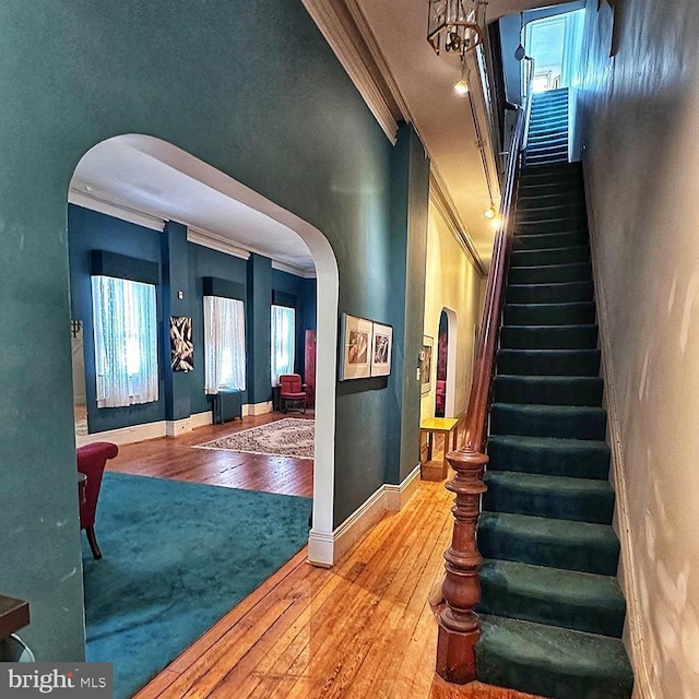 stairway with arched walkways, ornamental molding, and hardwood / wood-style flooring