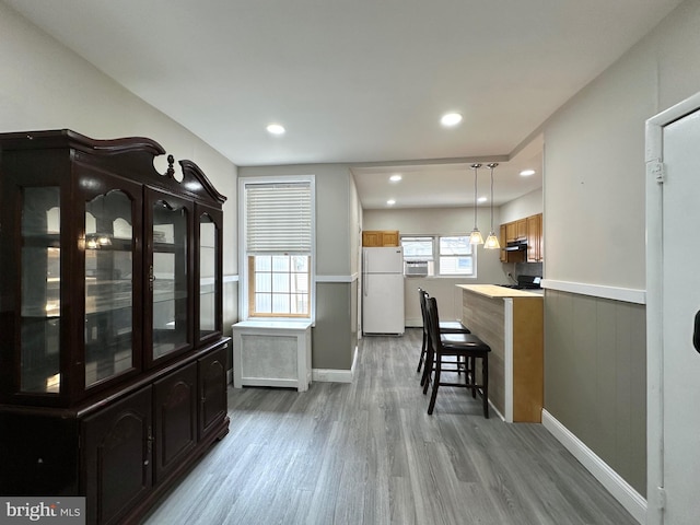 kitchen featuring light hardwood / wood-style floors, a breakfast bar, white refrigerator, kitchen peninsula, and pendant lighting