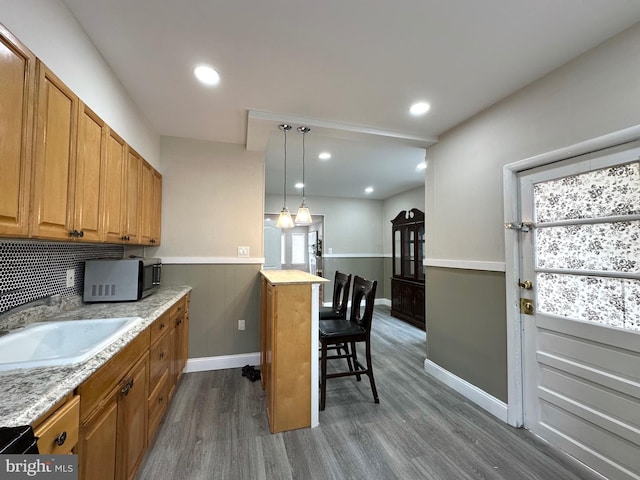 kitchen featuring dark wood-type flooring, sink, a kitchen bar, hanging light fixtures, and decorative backsplash