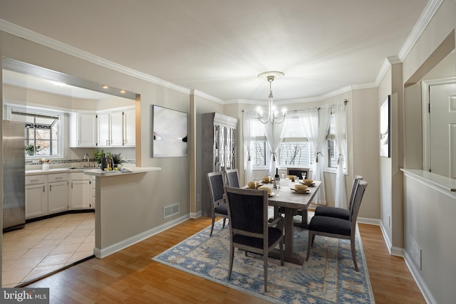 dining room featuring crown molding, light hardwood / wood-style flooring, sink, and an inviting chandelier