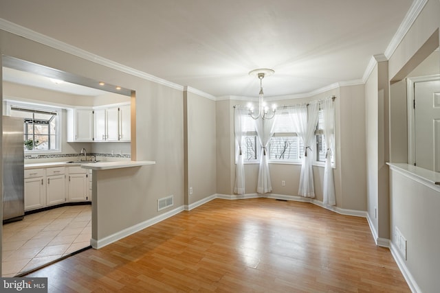 unfurnished dining area with crown molding, light hardwood / wood-style flooring, sink, and an inviting chandelier