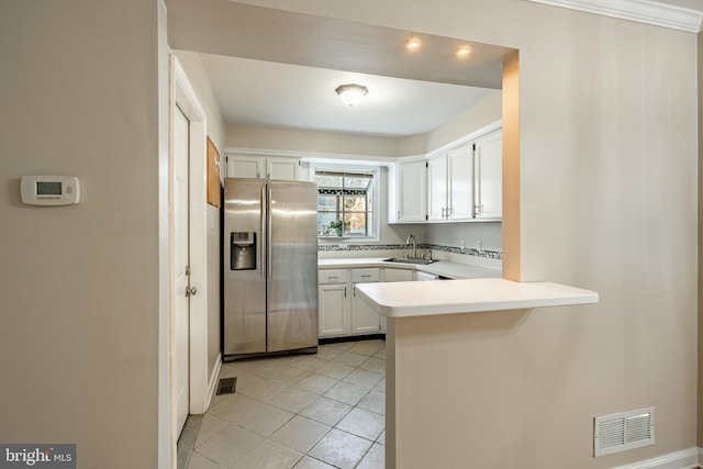 kitchen featuring sink, light tile patterned flooring, stainless steel refrigerator with ice dispenser, kitchen peninsula, and white cabinets