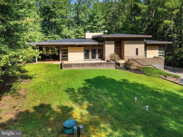 back of house with brick siding, a chimney, a view of trees, a yard, and a patio area