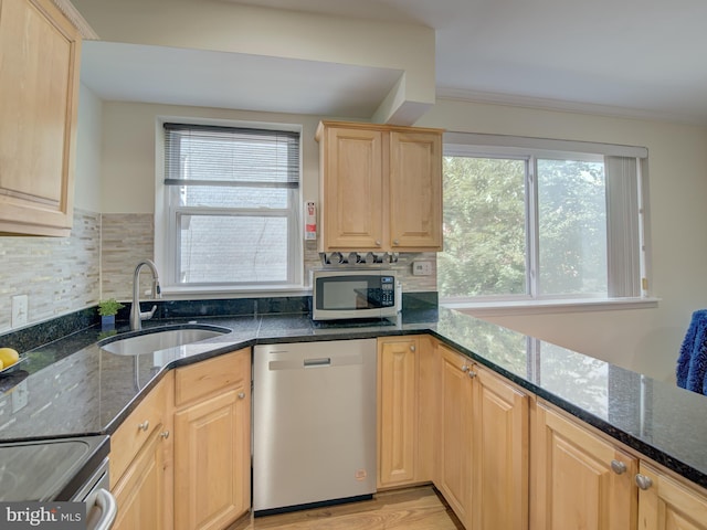 kitchen featuring light brown cabinets, stainless steel appliances, a sink, tasteful backsplash, and dark stone countertops