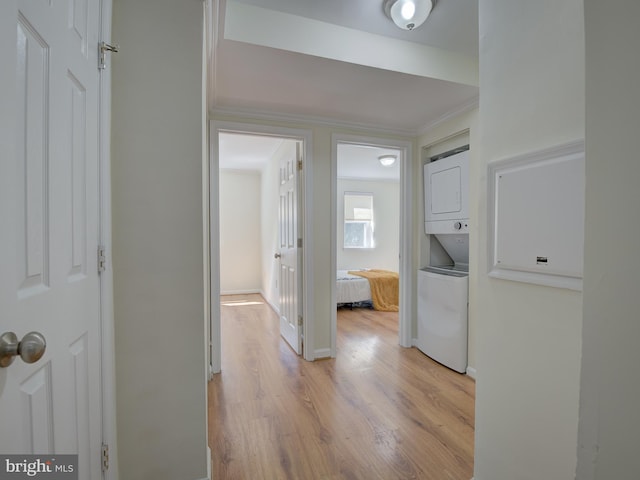 corridor featuring stacked washer and dryer, crown molding, light wood-style flooring, and baseboards