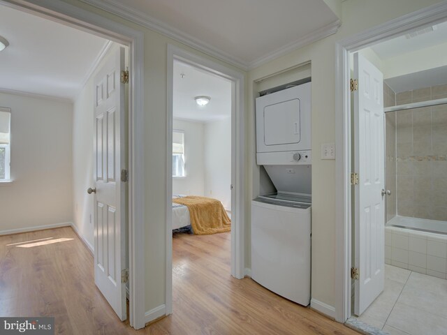 hall featuring light wood-style floors, baseboards, crown molding, and stacked washing maching and dryer