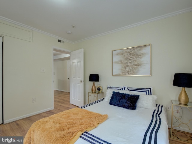 bedroom featuring ornamental molding, light wood-type flooring, visible vents, and baseboards